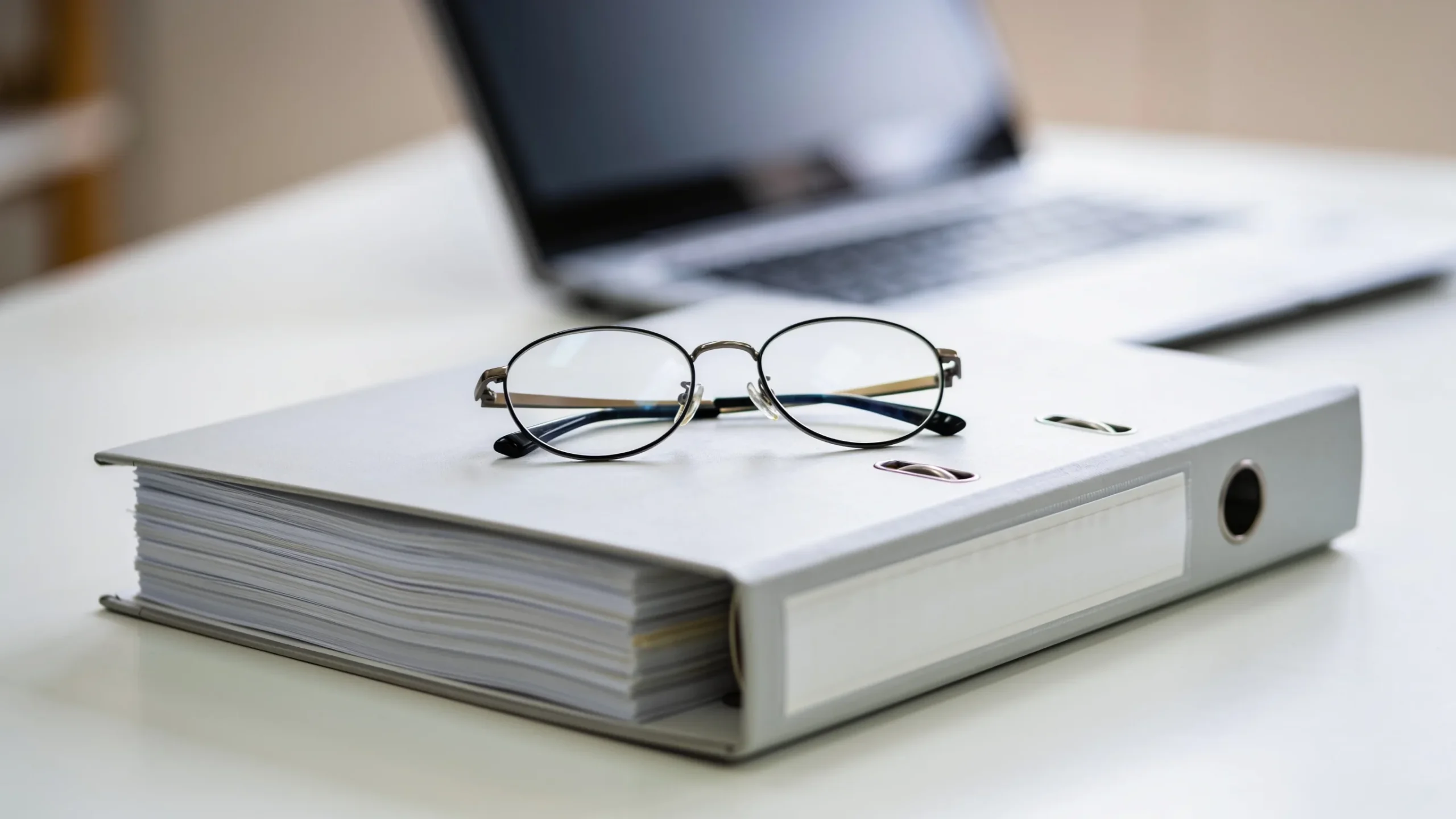 Convenio encuadernado de cientos de paginas con unas gafas encima y el portatil al fondo
